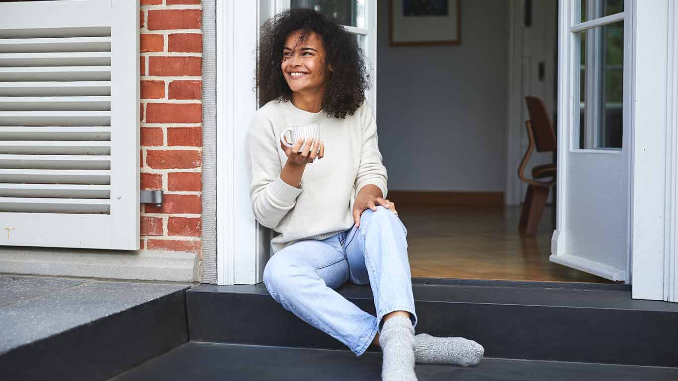 Vrouw zit op de veranda met een kopje en geniet.